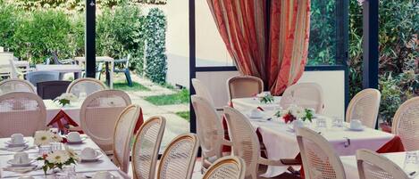 Un área de comedor al aire libre con mesas dispuestas para una comida, rodeada de sillas de mimbre y vistas a la vegetación.