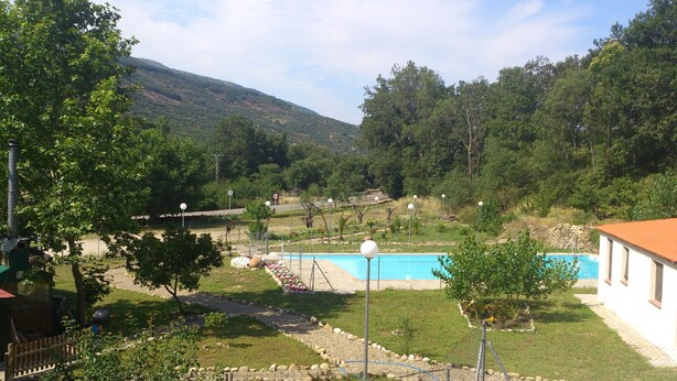 A residential area with a swimming pool, surrounded by trees and a hilly landscape.
