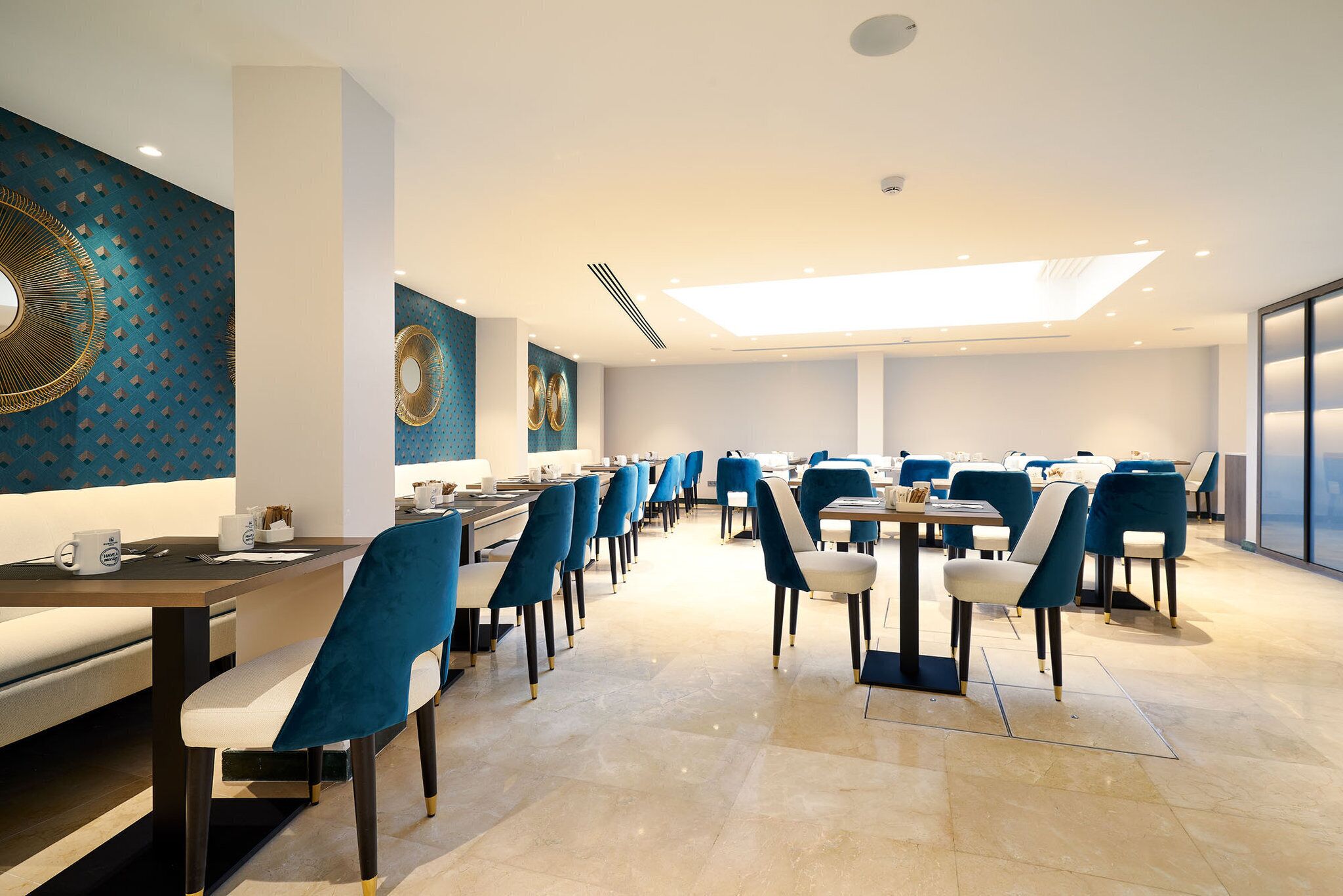 Un comedor moderno con sillas y mesas azules, una pared con diseño y un tragaluz.