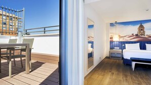 Habitación de hotel con cama, mesita de noche y ventana con vista a la ciudad.