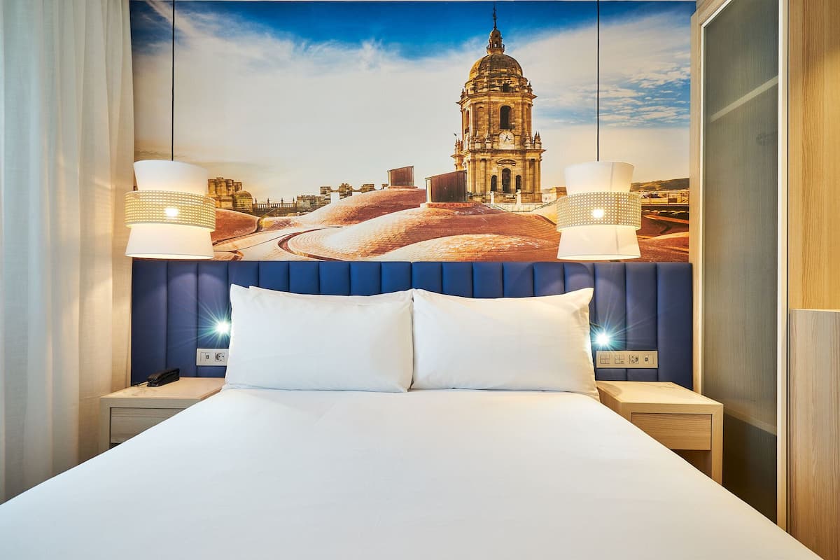 Ein Hotelzimmer mit einem Bett, zwei Nachttischen, einer Wandlampe und einem großen Stadtbild-Wandgemälde.