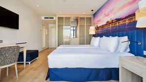 Una habitación de hotel moderna con una cama grande, un escritorio, un televisor y un mural con vistas a la ciudad.