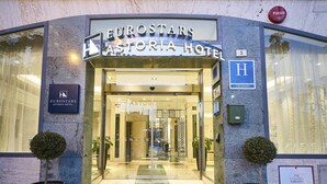 La entrada al Hotel Eurostars Astoria, con fachada de vidrio, un camino despejado y un cartel con el nombre del hotel.