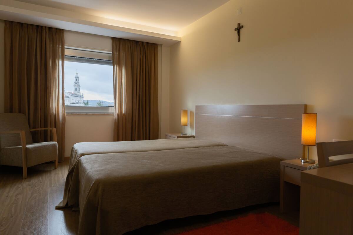 Ein Hotelzimmer mit zwei Betten, einem Sessel, einem Schreibtisch und einem Fenster mit Vorhängen.