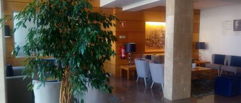 A lobby with a large potted tree, seating area, and a fire extinguisher.