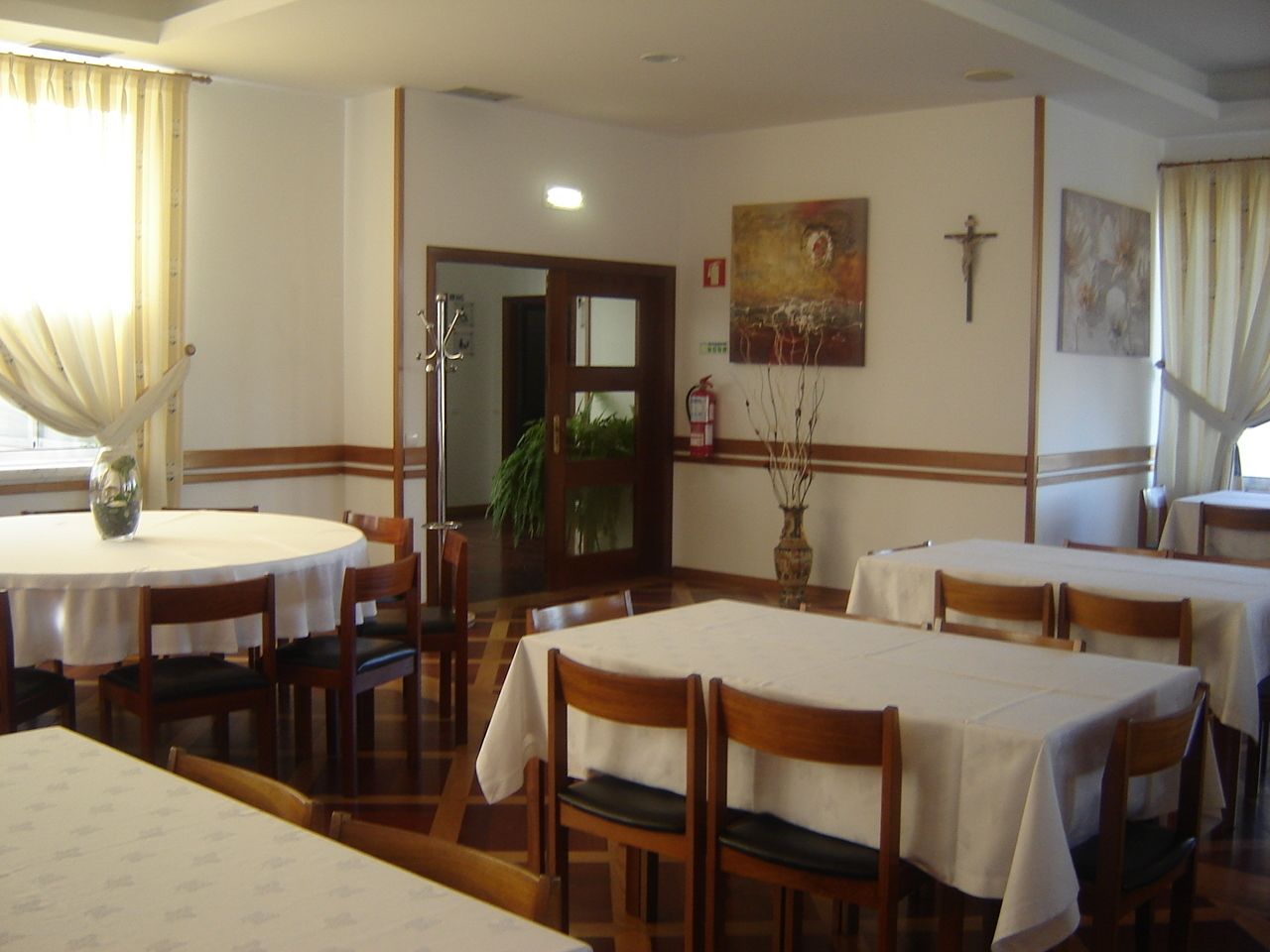 A dining area with round tables and chairs, a wooden floor, and a door leading to another room.