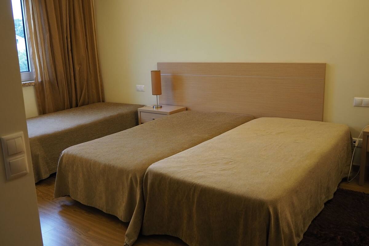 Ein Zimmer mit zwei Einzelbetten, einem Nachttisch mit Lampe und einem Fenster mit Vorhängen.