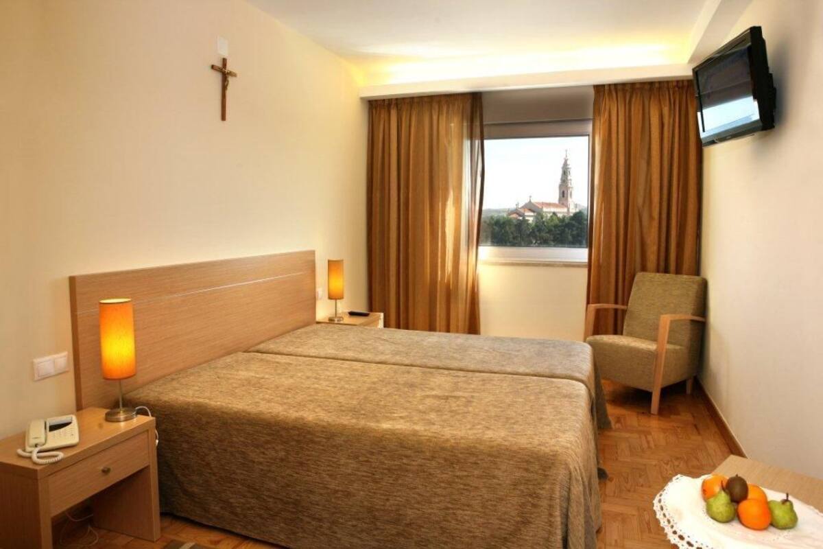 Ein Hotelzimmer mit Bett, Nachttischlampe, Stuhl, Fernseher und einem Fenster mit Vorhängen.