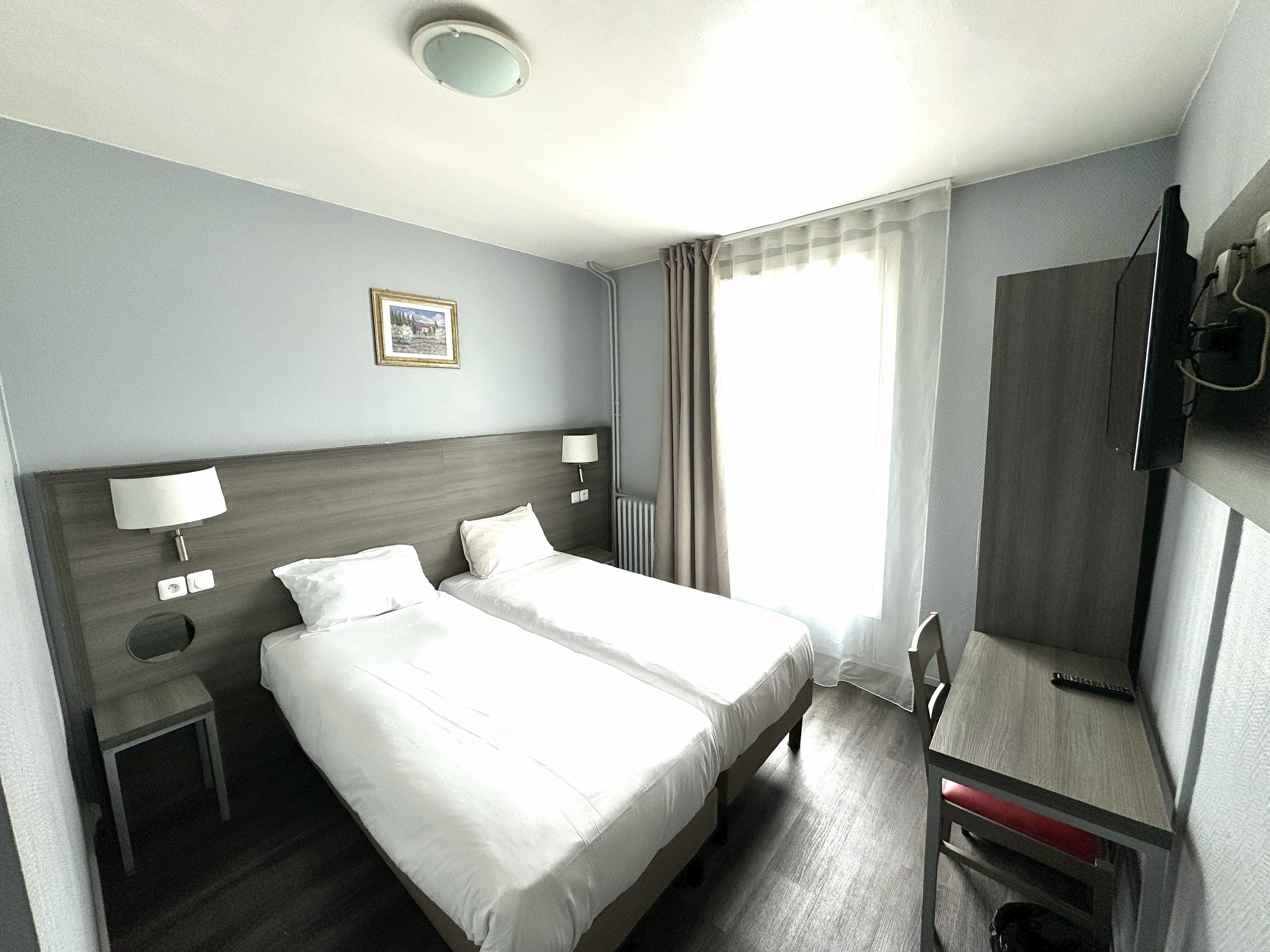 A hotel room with two beds, a desk, a chair, a television, and a picture on the wall.