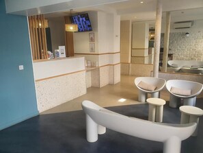 A reception area with a counter, seating, and a television. - Hipotel Paris Père Lachaise République (Paris)
