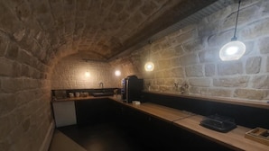 Cocina con paredes de piedra, encimera de madera, luces colgantes y una cafetera.