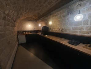 A stone-walled kitchen with a wooden countertop, hanging pendant lights, and a coffee machine. - Hipotel Paris Père Lachaise République (Paris)