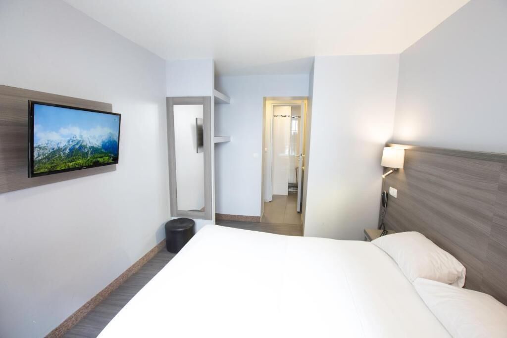 A hotel room with a bed, a mounted TV, a bedside table, and a door leading to a bathroom.