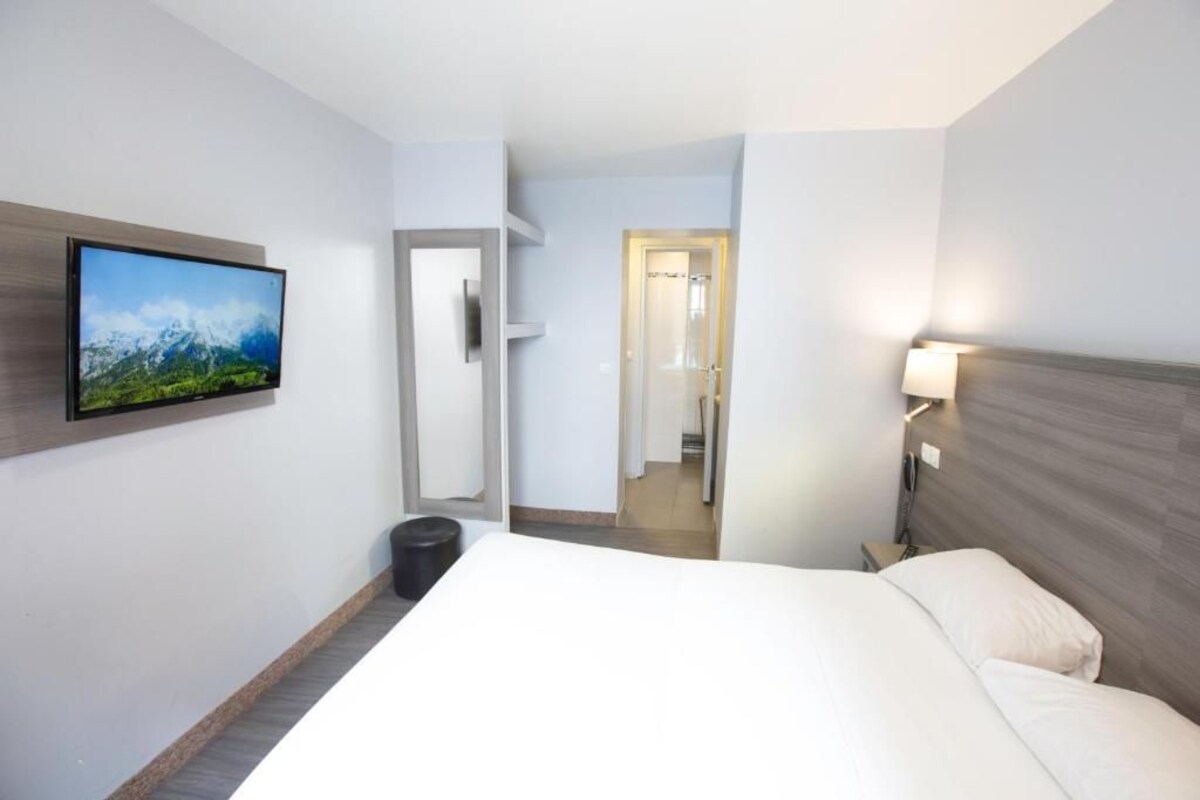 A hotel room with a bed, a mounted TV, a bedside table, and a door leading to a bathroom.