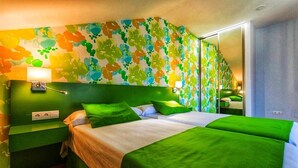 Quarto de hotel com esquema de cores verde, uma cama grande, uma mesa de cabeceira, um espelho e um papel de parede com padrão floral.