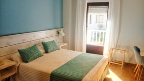 Quarto com cama, duas mesas de cabeceira, uma cadeira, janela com cortinas e varanda.