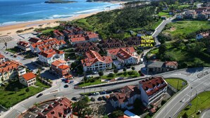 Vista aérea do Hotel Bemon Playa, destacando sua localização costeira com edifícios de telhado vermelho, uma praia e uma estrada que leva ao hotel.