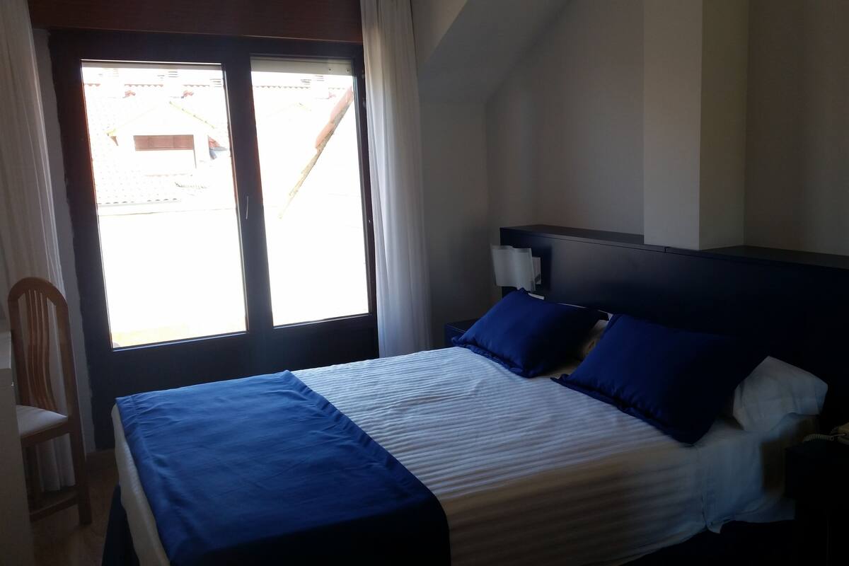 A bedroom with a bed, a chair, a bedside table, and a window.