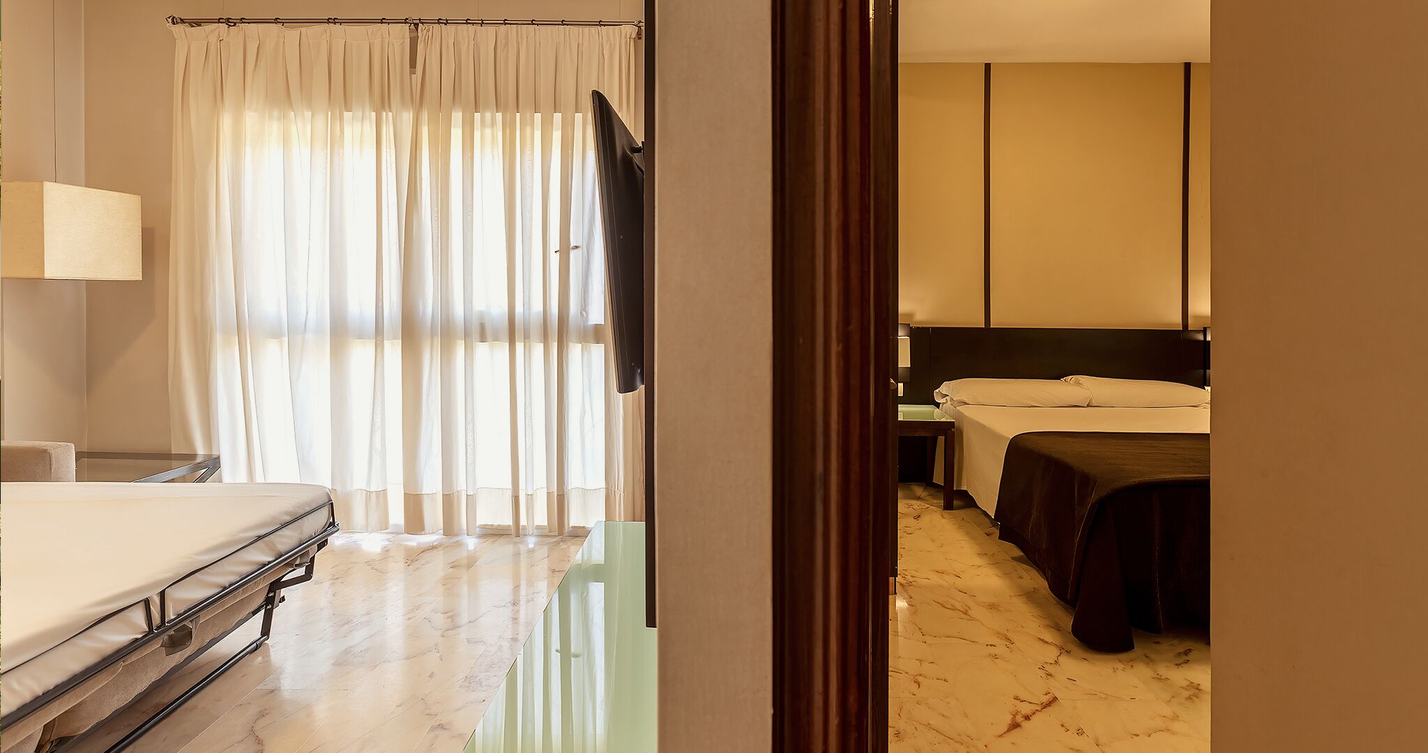 Une chambre d’hôtel avec un lit, une table de chevet, une lampe et une fenêtre avec des rideaux légers.