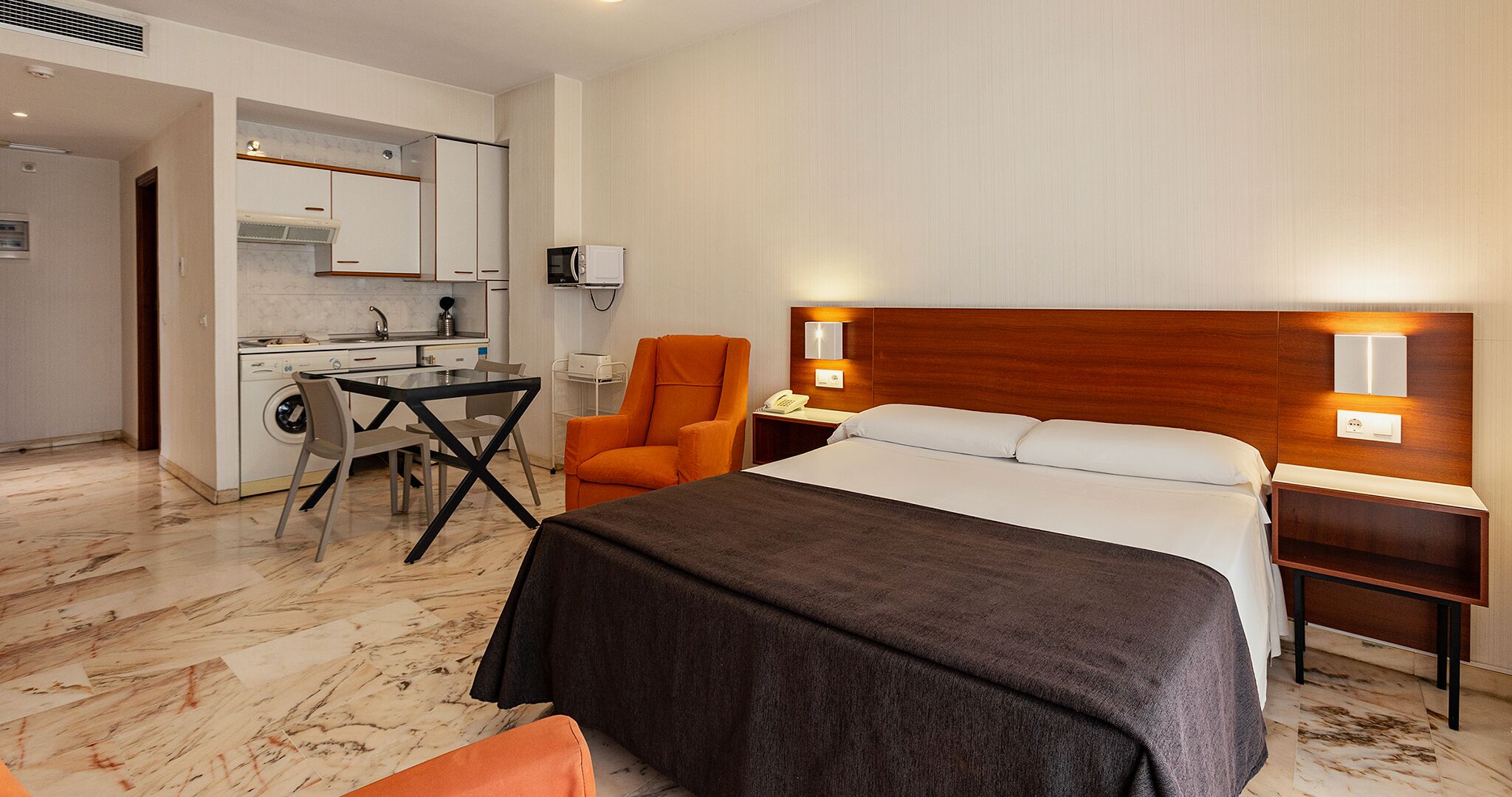 A hotel room with a bed, a desk, a chair, a microwave, and a washing machine.