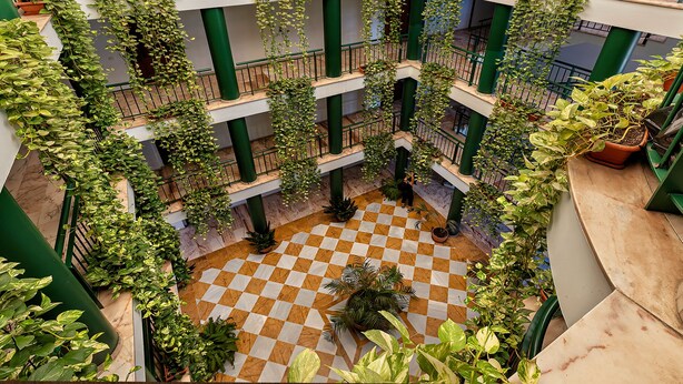 A multi-level atrium with a checkered floor, green railings, and various potted plants. - Apartamentos Vértice Bib Rambla (Seville)