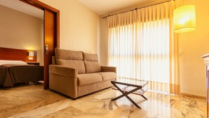 A hotel room with a sofa, a small table, a bed, and a window with curtains. - Apartamentos Vértice Bib Rambla (Seville)