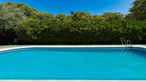 A clear blue swimming pool surrounded by lush green trees. - Apartamentos Vértice Bib Rambla (Seville)