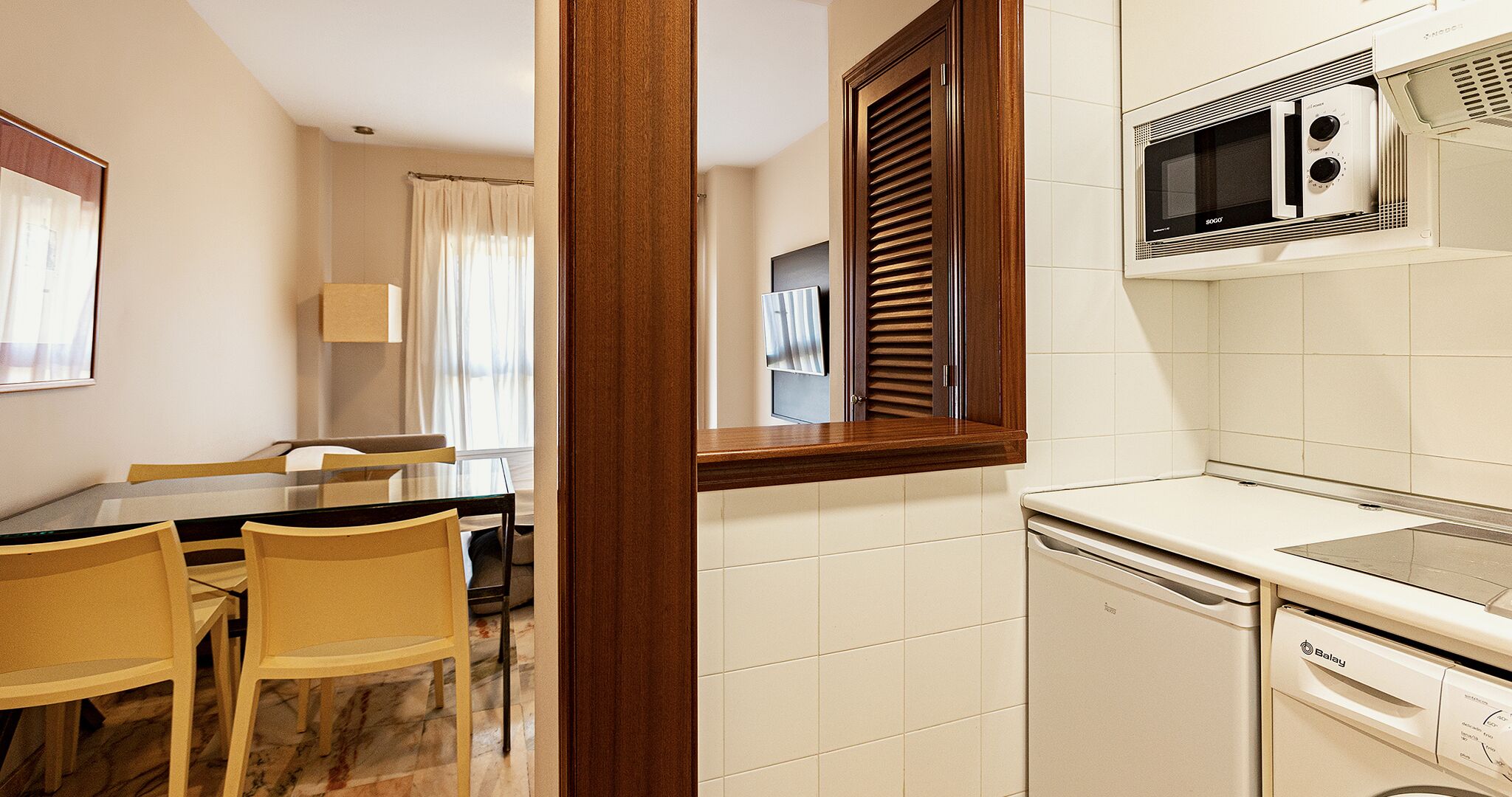 Een compacte keuken met een magnetron, vaatwasser en een eethoek met stoelen en een tafel.