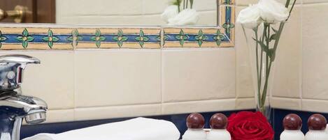 A bathroom with a tiled backsplash, a mirror, a sink, a towel, and toiletries.