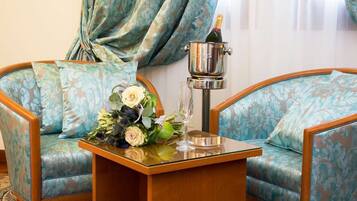 A room with two upholstered armchairs, a wooden side table with a floral arrangement and a champagne bottle, and a metallic object on the table.