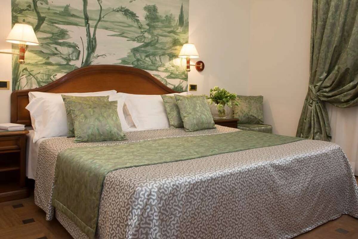 A neatly made bed with a patterned bedspread, two bedside lamps, a nightstand, and a wall mural.