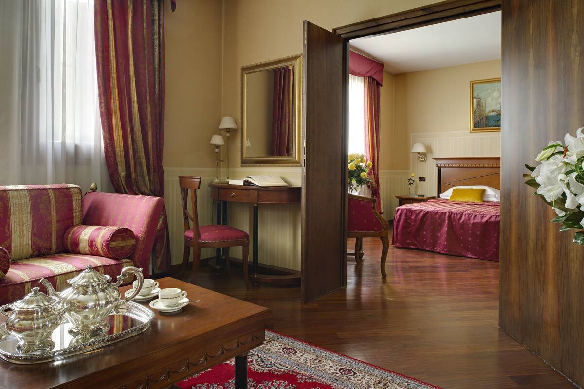 A hotel room with a sofa, a desk with a lamp, a bed with a yellow pillow, and a large mirror.
