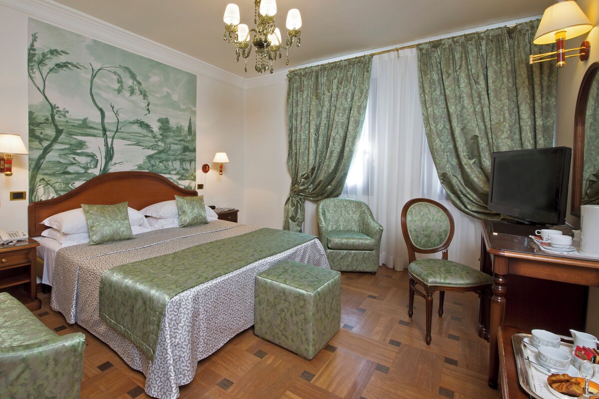 A hotel room with a large bed, a television, a desk with a tray of breakfast items, and a chair.