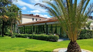 Un edificio con un patio techado, rodeado de césped cuidado y una palmera.