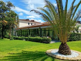 Un edificio con un patio techado, rodeado de césped cuidado y una palmera.