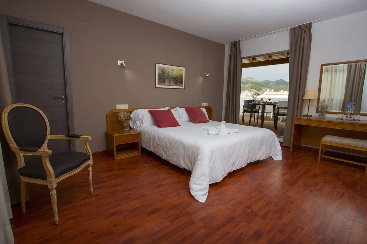 A hotel room with a bed, a chair, a desk, and a view of the outdoors.