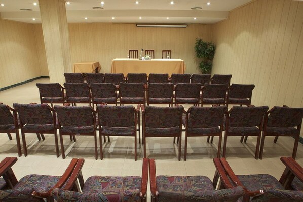 Un salón de conferencias con filas de sillas y una mesa en el centro, equipado con un proyector.