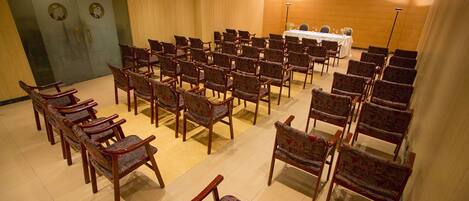 A conference room with rows of chairs facing a table with a white tablecloth and a speaker.