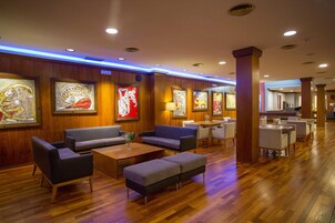 Un vestíbulo de hotel con paneles de madera, obras de arte en las paredes, zonas de estar y una recepción.