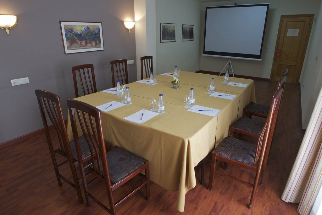 Una sala de conferencias con una larga mesa, sillas, una pantalla de proyector y cuadros en la pared.