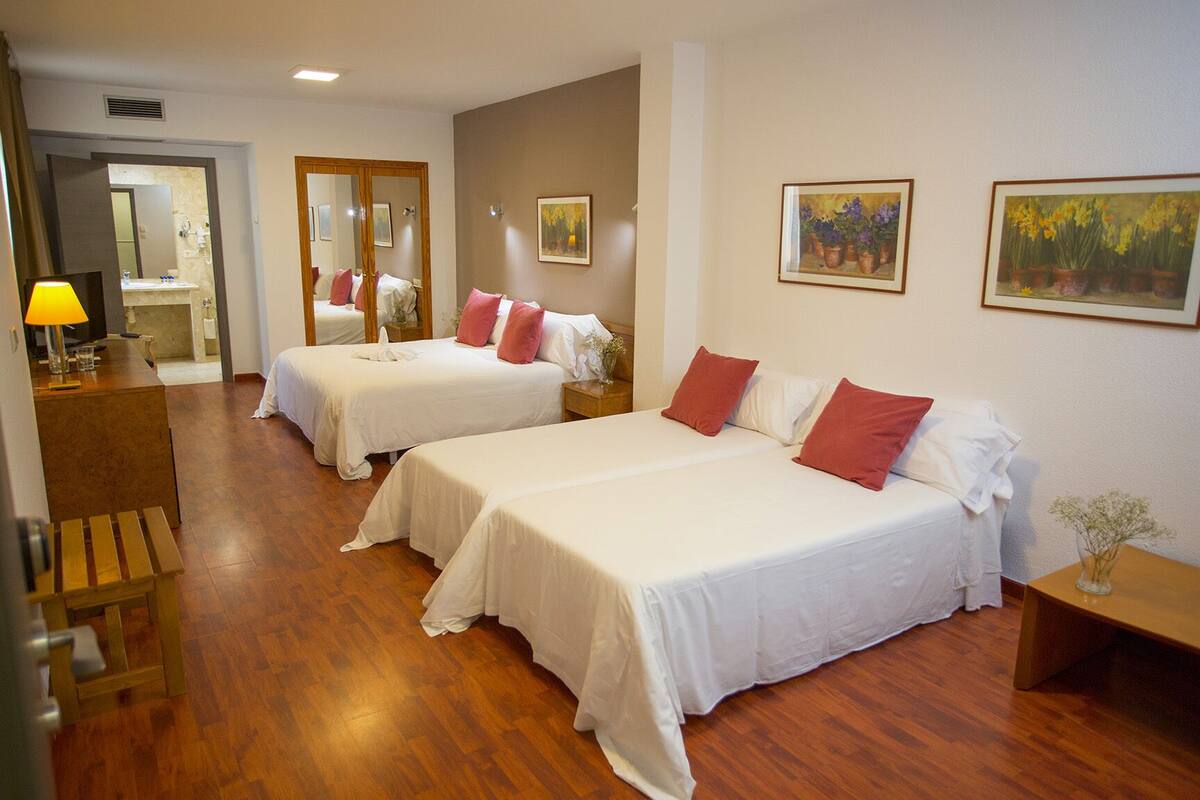 A hotel room with two beds, wooden flooring, a desk with a lamp, and artwork on the walls.