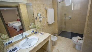 A bathroom with two sinks, a shower, and a toilet. There is a mirror above the sinks, and a towel rack is visible on the wall.