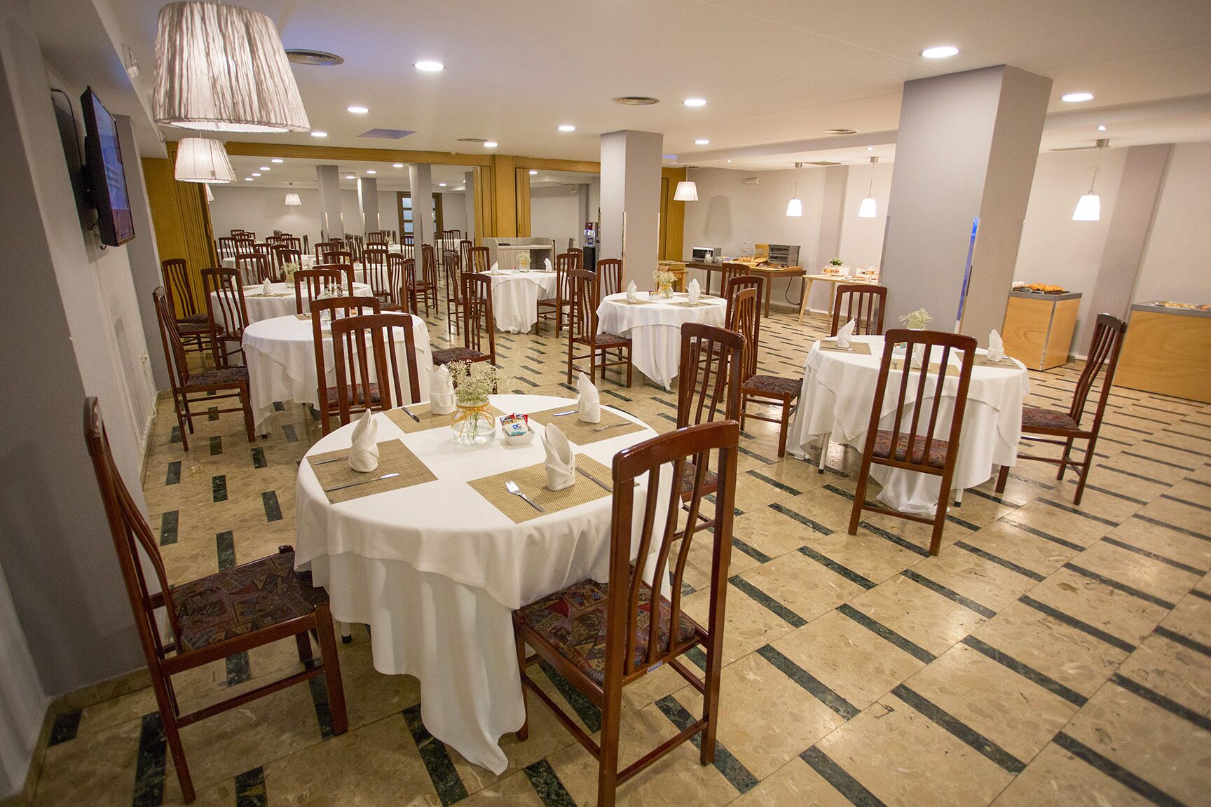 Un comedor con varias mesas redondas, cada una con mantel blanco, sillas de madera y centros de mesa.