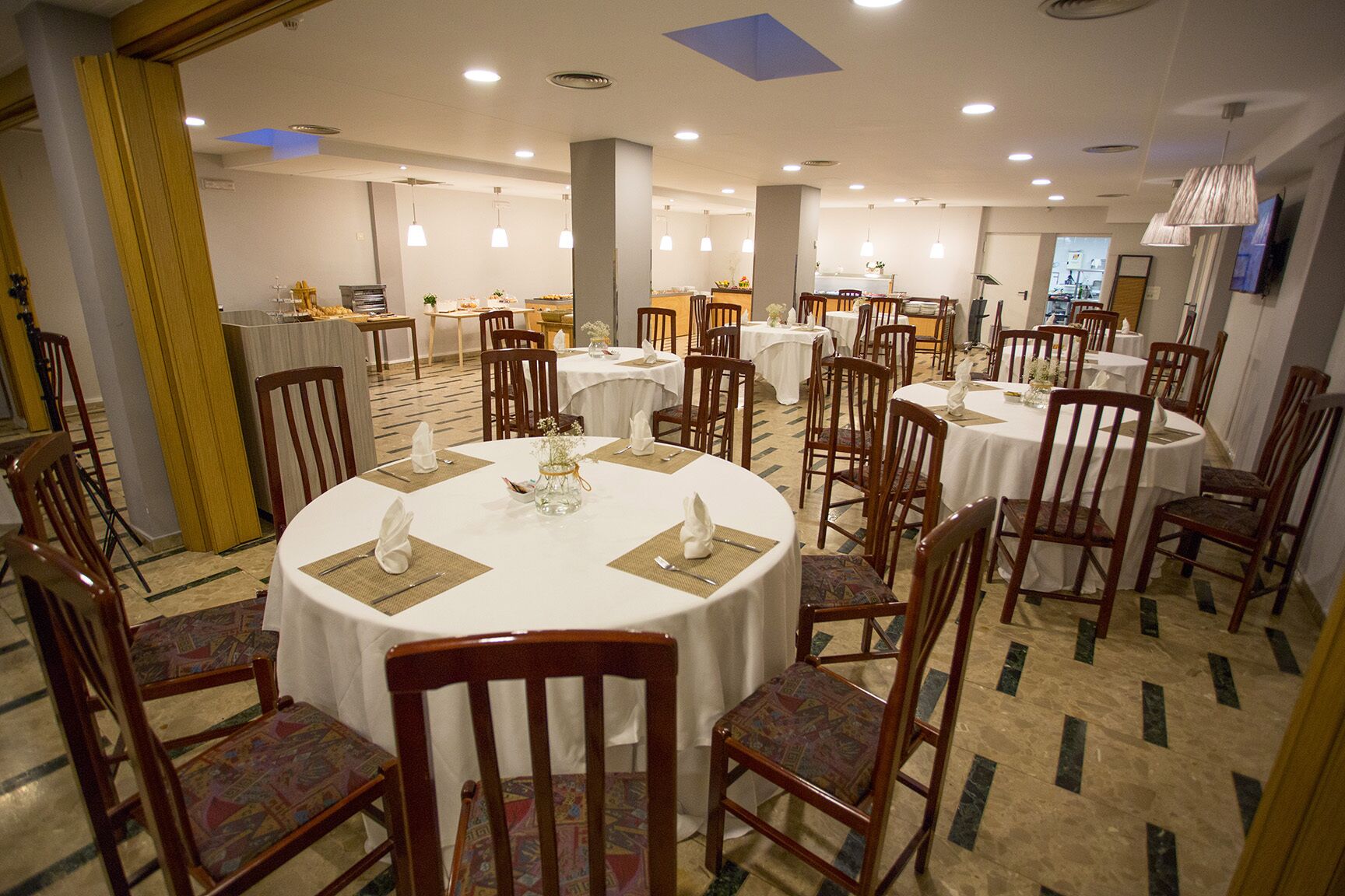 Un comedor con mesas redondas, sillas y piso de baldosas.