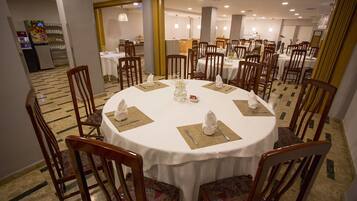 A dining area with round tables, wooden chairs, and white tablecloths.