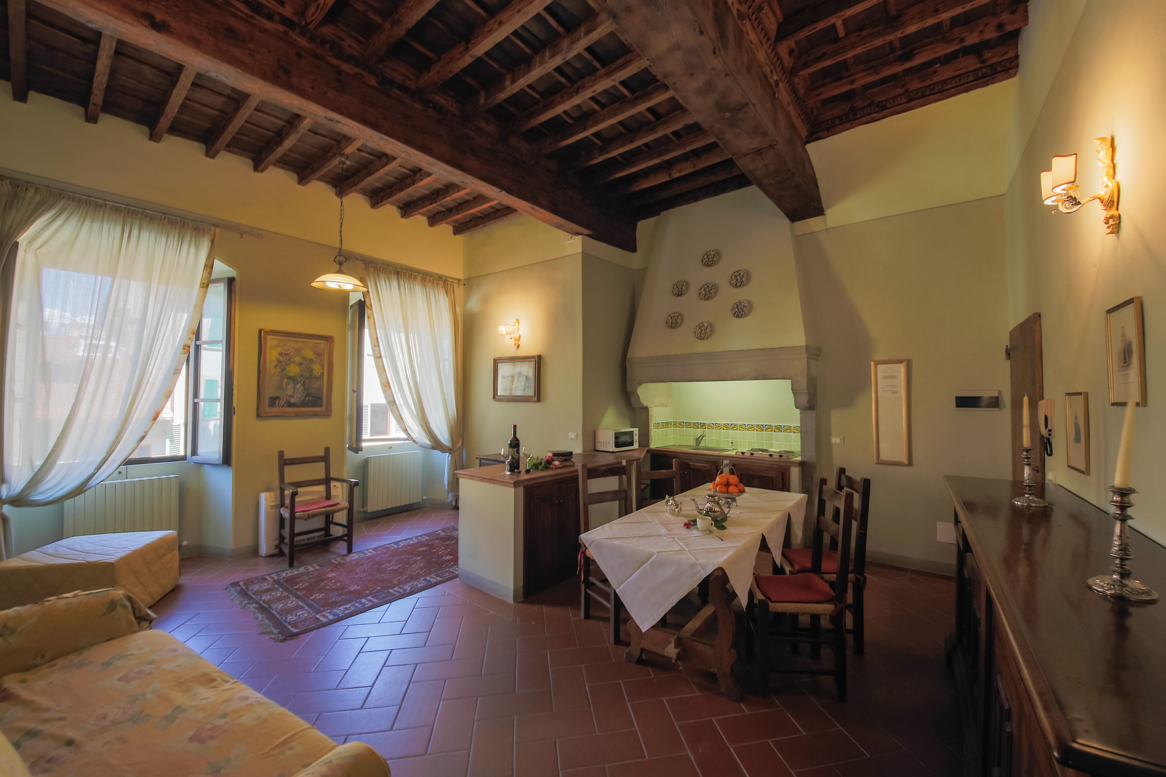 A cozy dining area with a table set for two, a wooden bench, and a kitchen in the background.
