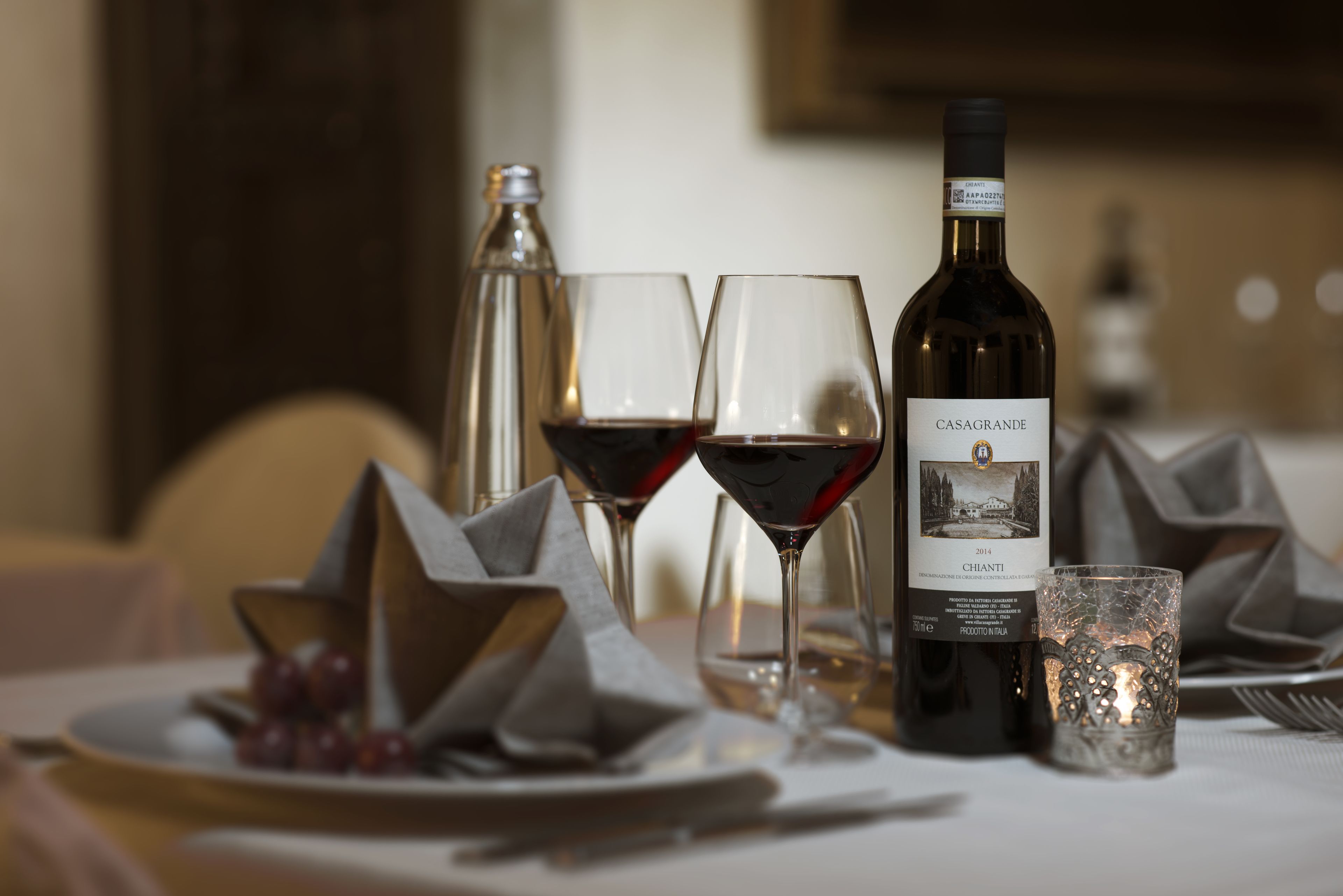 Une table dressée avec une bouteille de vin, deux verres à vin, une bougie et une assiette de raisins.