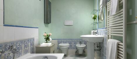 A bathroom with a bathtub, toilet, bidet, and sink, featuring blue and white tiles and a green wall.