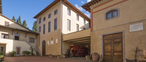 Une cour intérieure avec un bâtiment doté d’une grande porte en bois et d’une enseigne, ainsi que des plantes en pot et un sol pavé de pierres.