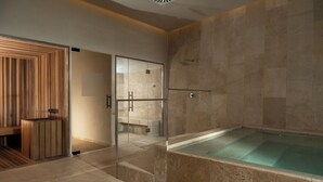 Un área de spa moderna con sauna de madera, ducha con cerramiento de vidrio y piscina con suelo de mármol.